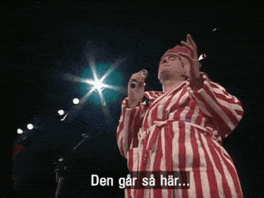 a man in a red and white striped robe singing into a microphone with the words den går sa har
