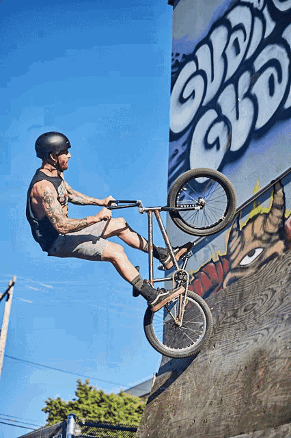 a man wearing a helmet is riding a bike on a ramp with graffiti on the wall behind him