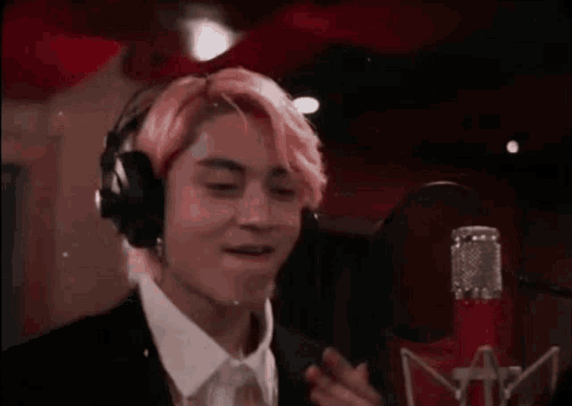 a man with pink hair is singing into a microphone in a recording studio .