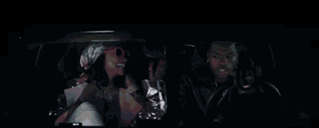 a man and a woman are sitting in a car and the woman is wearing pink sunglasses