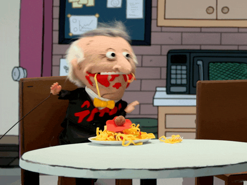 a puppet is sitting at a table with a plate of spaghetti on it