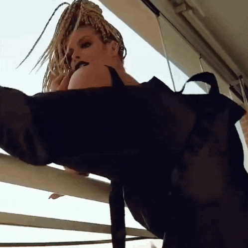 a woman with dreadlocks is standing on a balcony looking out the window