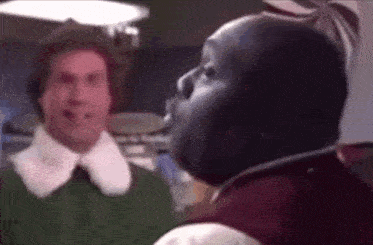 two men are standing next to each other in a room and one of them is wearing a red jacket .