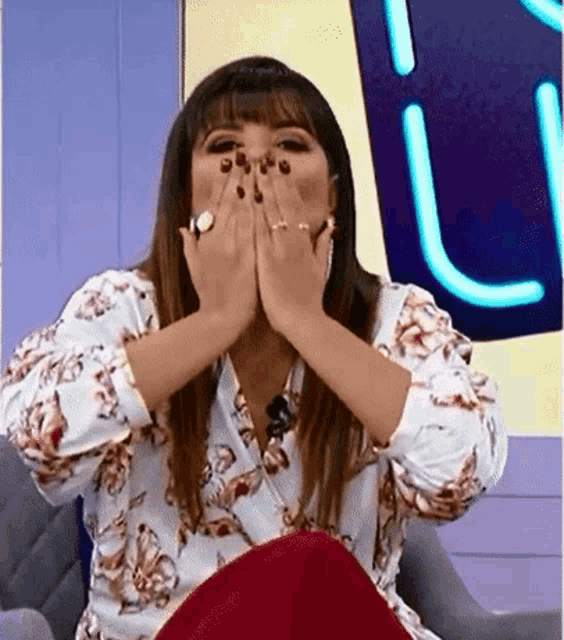 a woman in a floral shirt is covering her mouth with her hands .