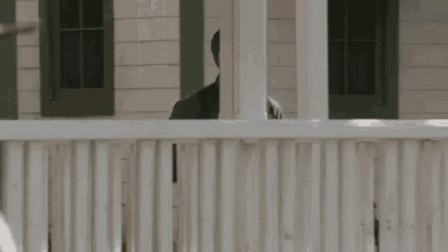 a man is standing behind a white fence looking over it .