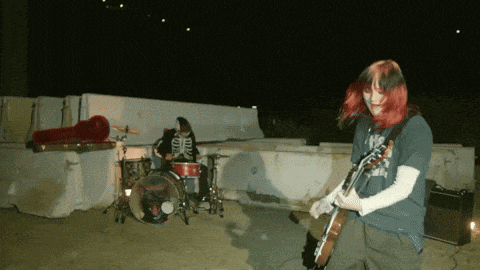 a woman with red hair is playing a guitar while a man plays drums