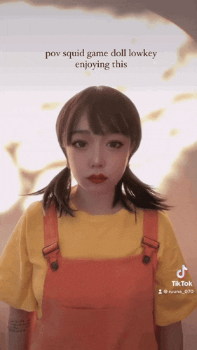 a girl in a yellow shirt and orange overalls with the caption pov squid game doll lowkey enjoying this on the bottom