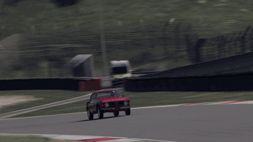 a red car is driving on a race track with a fence in the background