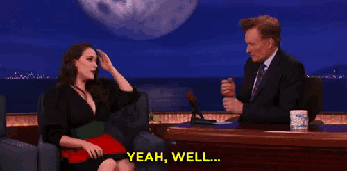 a man and a woman are sitting at a table and the man is saying yeah well