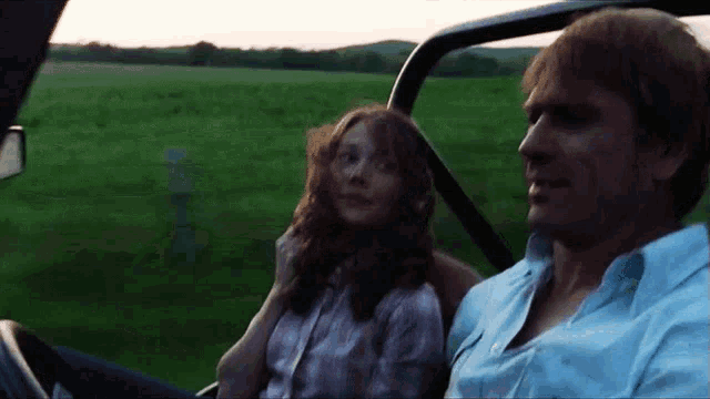 a man and a woman are sitting in a car in a field