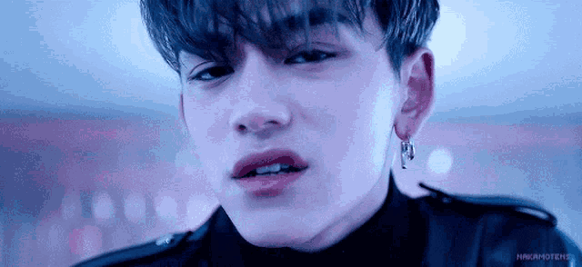 a close up of a young man wearing a black jacket and earrings .