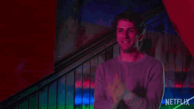 a man in a purple sweater applauds in front of a netflix logo