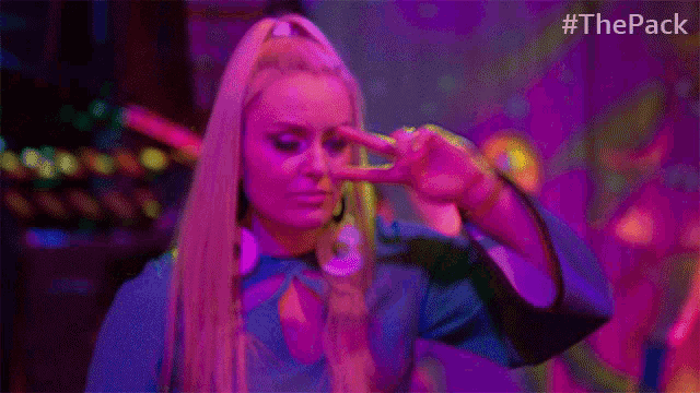 a woman making a peace sign in front of a purple background with #thepack at the bottom