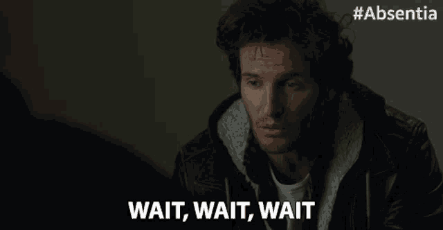 a man in a leather jacket says wait wait wait in a dark room