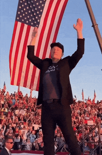 a man stands in front of a large american flag with his arms in the air