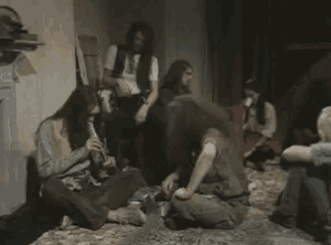 a man with long hair is sitting on the floor in a room with a group of people .