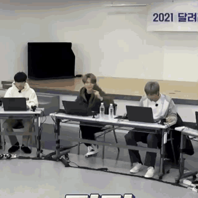 a group of people are sitting at tables with laptops in front of a sign that says 2021 .