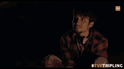 a man in a plaid shirt is sitting in the dark and talking to someone .