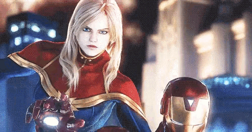 a woman in a superhero costume is standing next to a man in an iron man helmet .