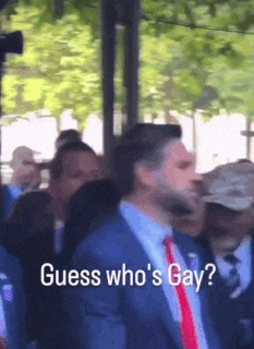 a man in a suit and tie is standing in front of a crowd and says " guess who 's gay "