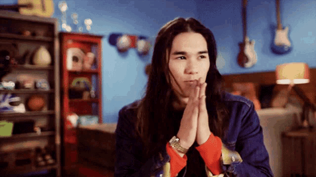 a man with long hair is praying with his hands folded in front of him