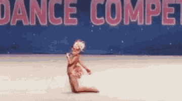 a little girl is kneeling on the floor in front of a dance competition sign