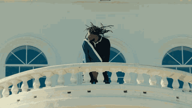 a man with dreadlocks stands on a balcony overlooking a building