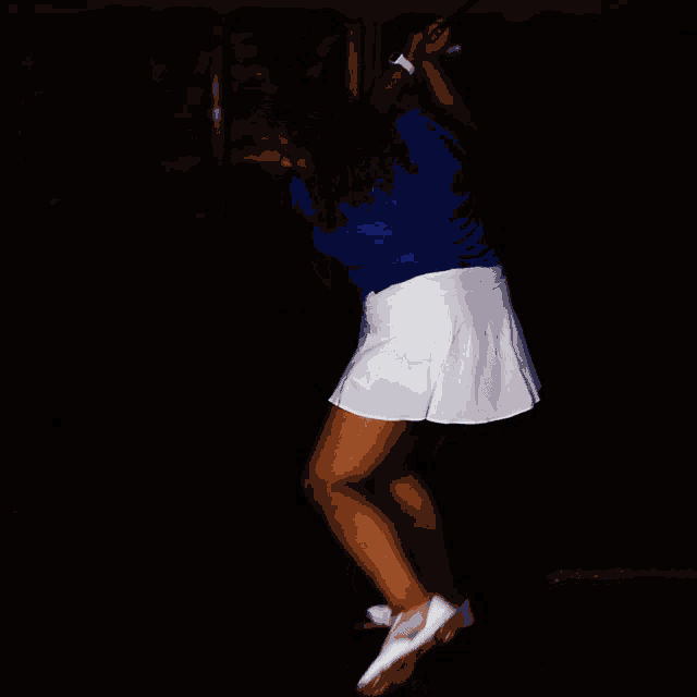 a girl in a blue shirt and white skirt swings a tennis racket