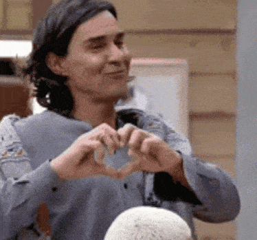 a man is making a heart shape with his hands and smiling .