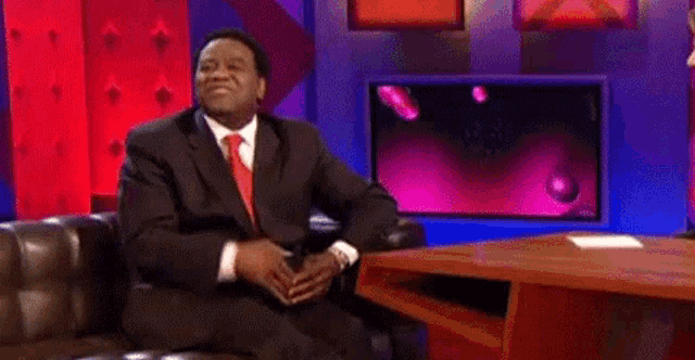 a man in a suit and tie is sitting in a chair on a stage .