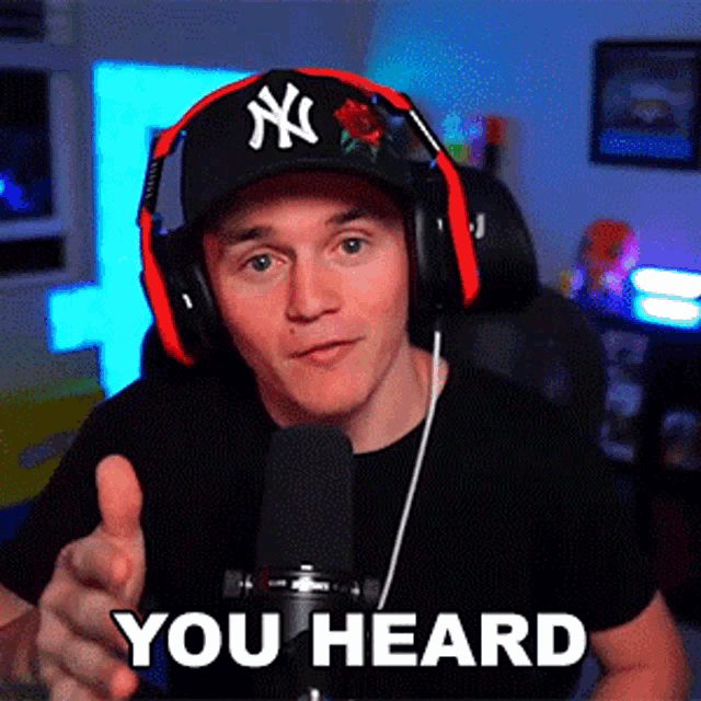 a man wearing headphones and a ny hat is pointing at the camera and says you heard