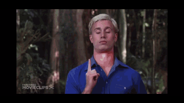a man in a blue shirt is standing in a forest with his eyes closed .