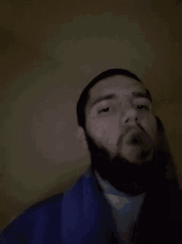 a man with a beard is wearing a blue shirt and making a funny face .