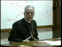 a priest sits at a desk in front of a whiteboard that says " abc "