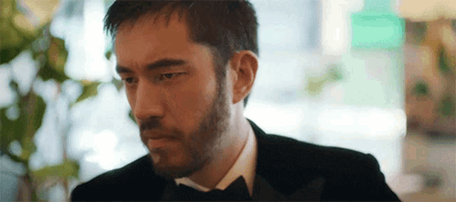a man with a beard is wearing a black tuxedo