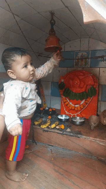 a baby playing with a bell in front of a statue