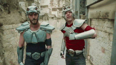 two men dressed in armor are walking down a street .