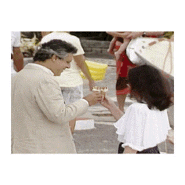 a man in a tan suit is giving a woman a sandwich