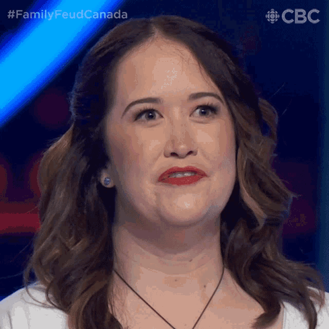 a woman with a white shirt and red lipstick looks at the camera with the words family feud canada behind her