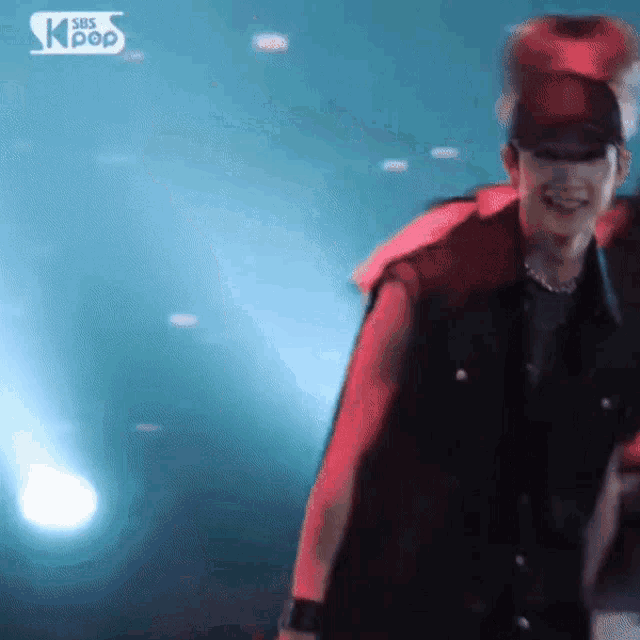 a man in a red hat is dancing in front of a sbs kpop sign