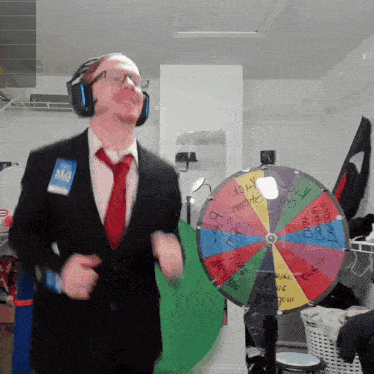 a man in a suit and tie is dancing in front of a colorful spinning wheel that says " lottery " on it