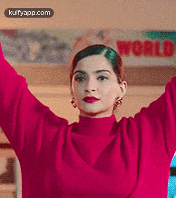 a woman in a pink sweater is standing with her arms in the air .