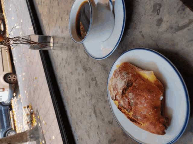 a cup of coffee sits on a saucer next to a croissant on a plate