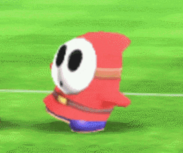 a shy guy from mario bros is jumping in the air on a green field .