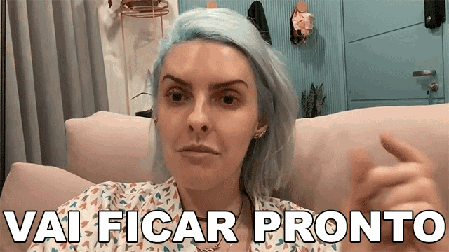 a woman with blue hair is sitting on a couch with the words vai ficar pronto behind her