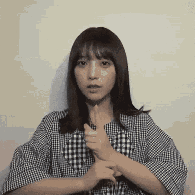 a young woman in a plaid shirt is making a silly face while holding her hands together .