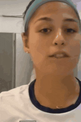 a woman wearing a headband and a white shirt looks at the camera