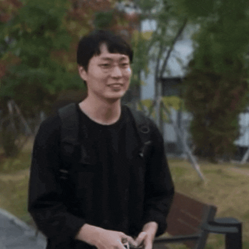 a man wearing a black shirt and a backpack is standing in front of a bench .