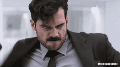 a man in a suit and tie with a mustache is looking at the camera .