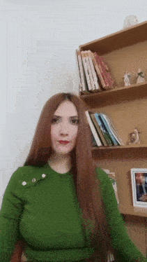 a woman in a green sweater stands in front of a bookshelf filled with books
